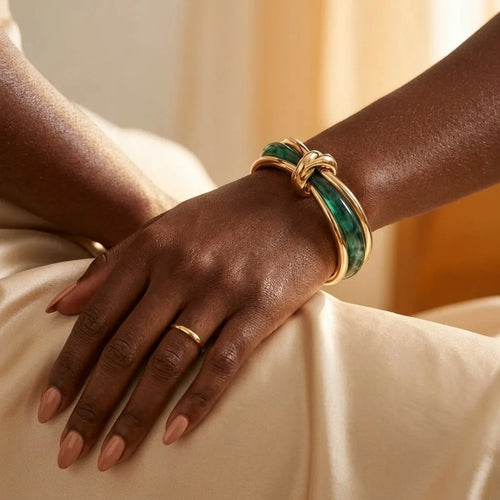 MAYA 01 Amalfi knot bangle in Malachite Gold worn on the wrist, resting on champagne satin