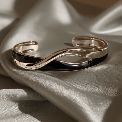 MAYA 01 Cannes crossover cuff in Onyx Silver, a glossy black band twisting over a polished silver band, on silver-grey satin