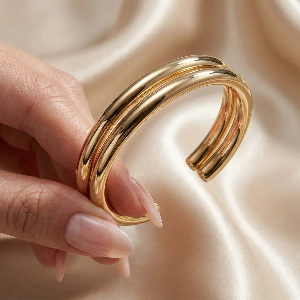 MAYA 01 Ravello double band cuff in Polished Gold held in the hand over champagne satin