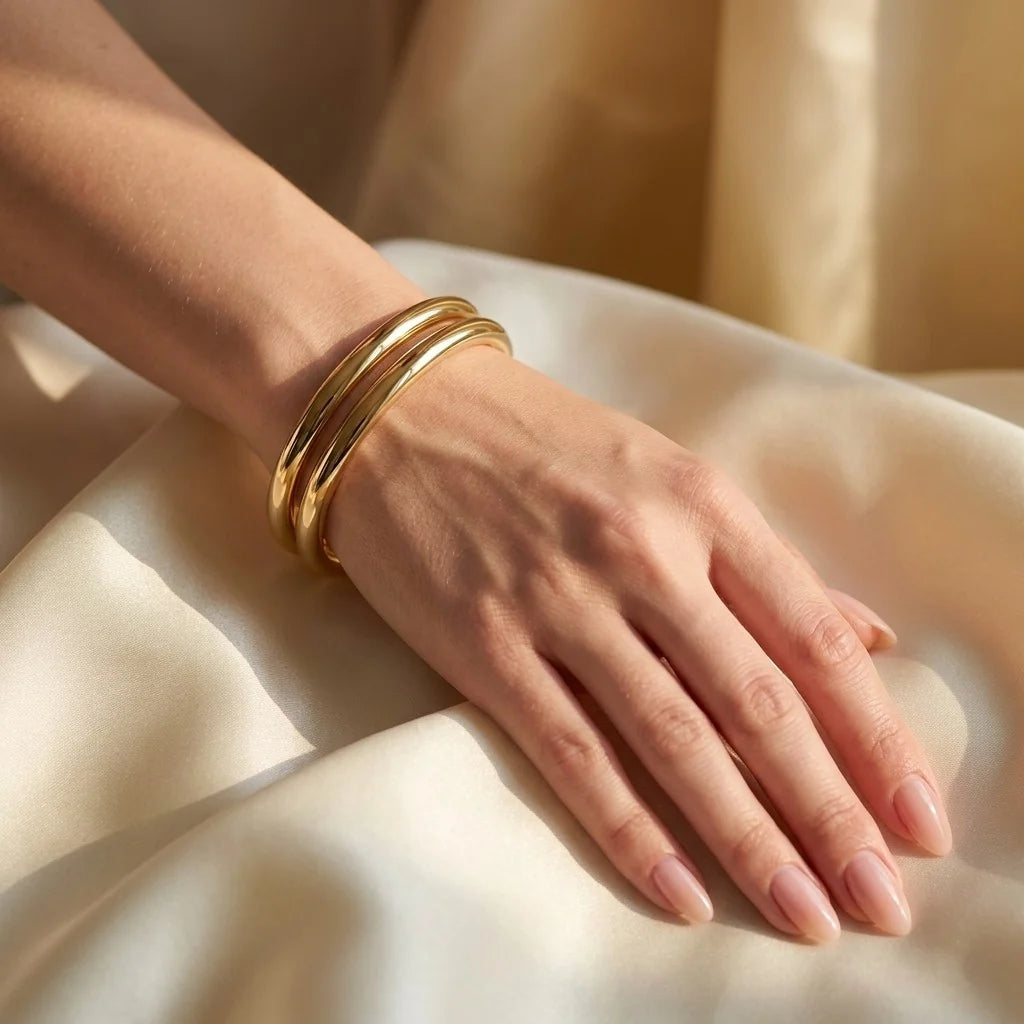 MAYA 01 Ravello double band cuff in Polished Gold worn on the wrist in warm light over ivory silk