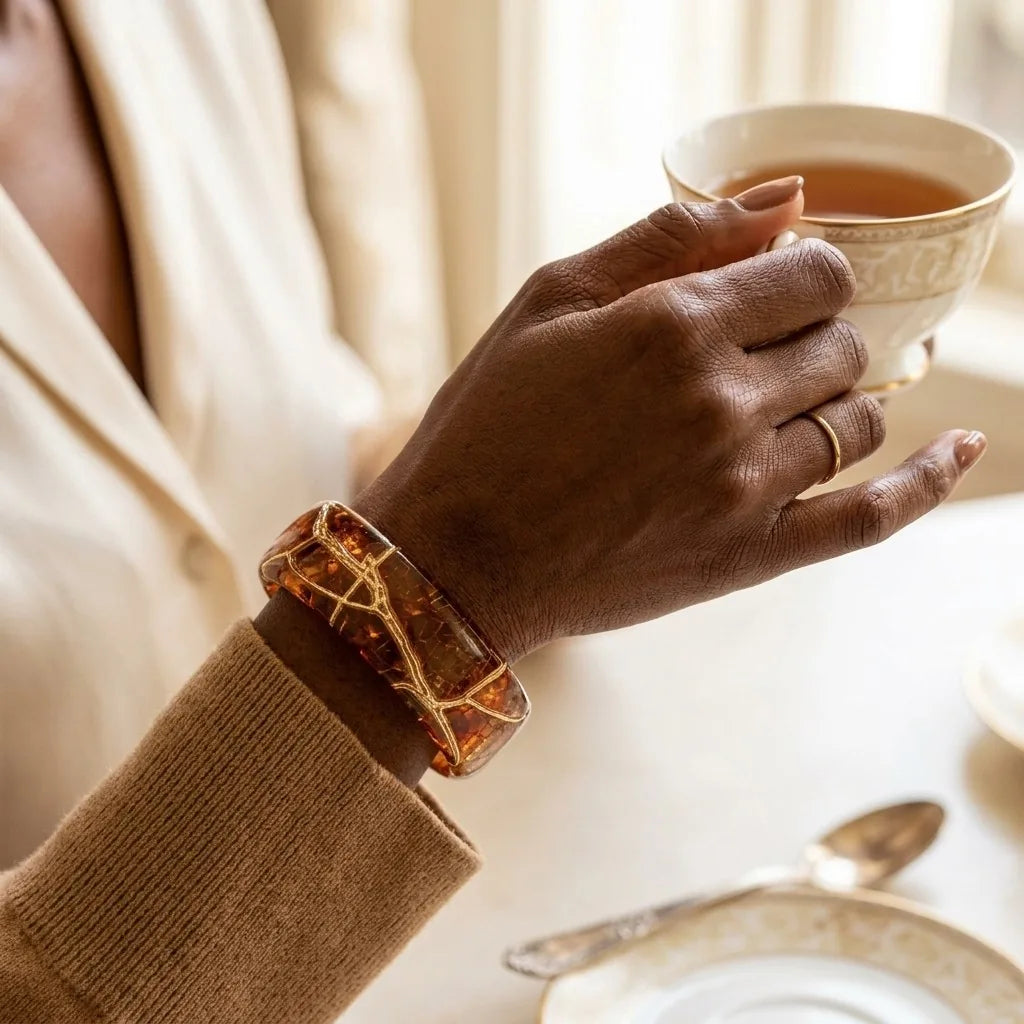 MAYA 01 Sorrento cuff in Honey Amber worn with a camel knit, holding a porcelain teacup