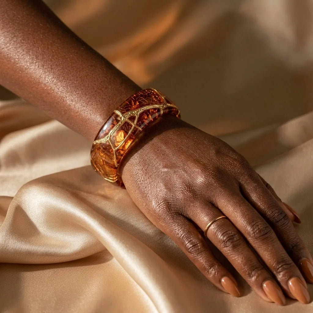 MAYA 01 Sorrento cuff in Honey Amber worn on the wrist with a fine gold ring, resting on champagne satin